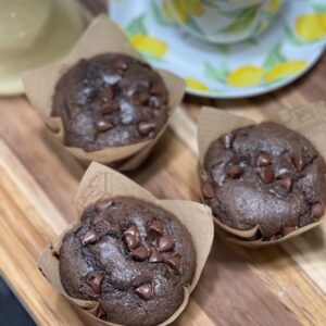 Chocolate muffins with chocolate chips and a floral teacup on a wooden board.